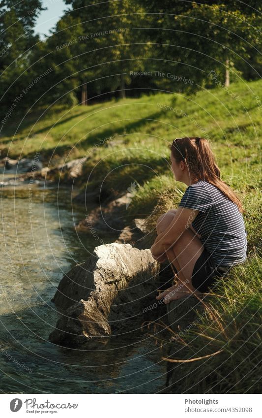 Junge Frau sitzt am Ufer eines kleinen Flusses und schaut in die Ferne Kontrast Schatten Außenaufnahme Farbfoto Vertrauen Glück sitzen genießen Bach Erholung