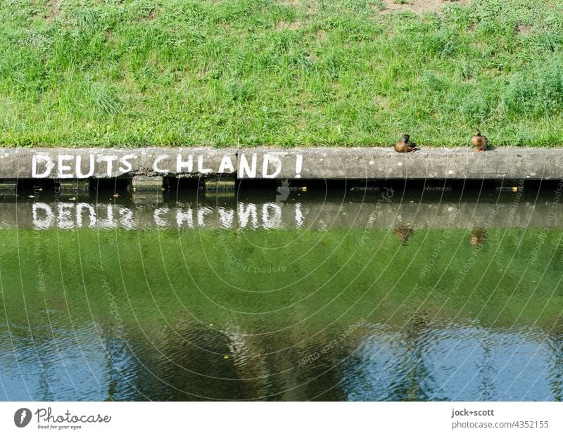 Reflexion in Deutschland! mit Enten Großbuchstabe Straßenkunst Wort Reflexion & Spiegelung Uferbefestigung Treptow Neukölln Berlin Wasseroberfläche Gras