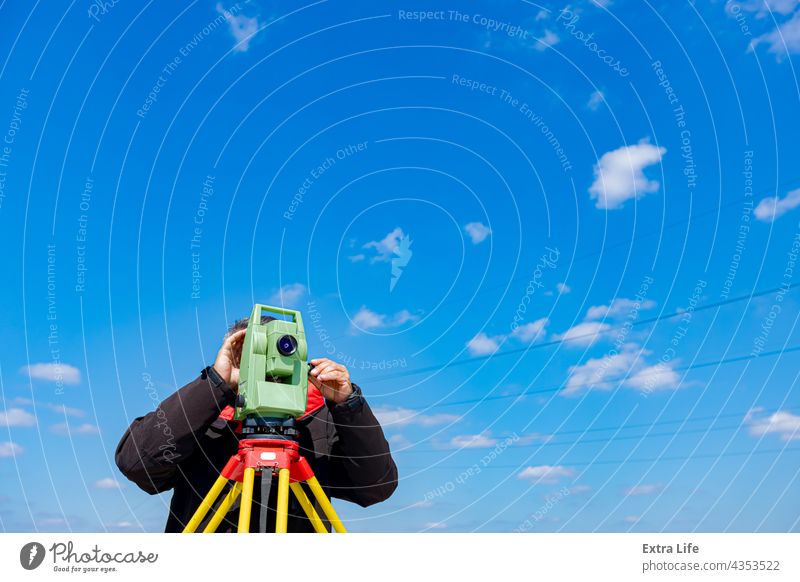 Bauingenieur, Geodät arbeitet mit Totalstation auf einer Baustelle, blauer Himmel im Hintergrund Genauigkeit Vorrichtung Überprüfung Tiefbau Wolken wolkig