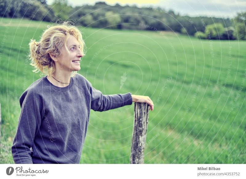 Porträt einer jungen reifen kaukasischen Frau, die im Freien steht und sich auf einen Pfahl im Frühling stützt. Lebensstile Menschen Frauen blond nur Lifestyle