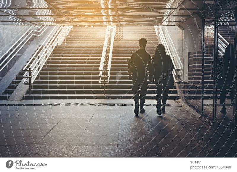 Silhouetten von Menschen. Menschen in unterirdischer Kreuzung. Blick von hinten. Pärchen von jungen Leuten auf dem Zebrastreifen. Das Paar hält sich an den Händen und geht durch die Stadt. Unbekannte Personen. Straßenfoto