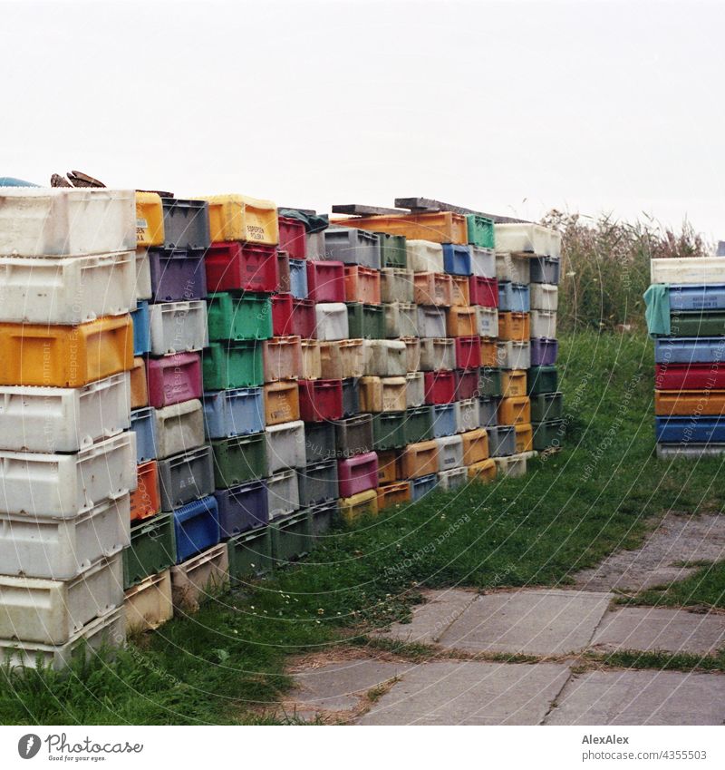 Fischkisten- Tetris- Mosaik - gestapelte, bunte Fischkisten auf einem Stück Rasen neben dem Weg Kiste Plastik Kunststoff gesapelt Stapel krumm und schief rot