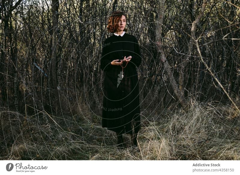 Emotionslose Frau in schwarzem Kleid zu Halloween im Wald stehend anketten durchkreuzen Outfit Mysterium Feiertag Wälder Herbst Phantasie Veranstaltung dunkel