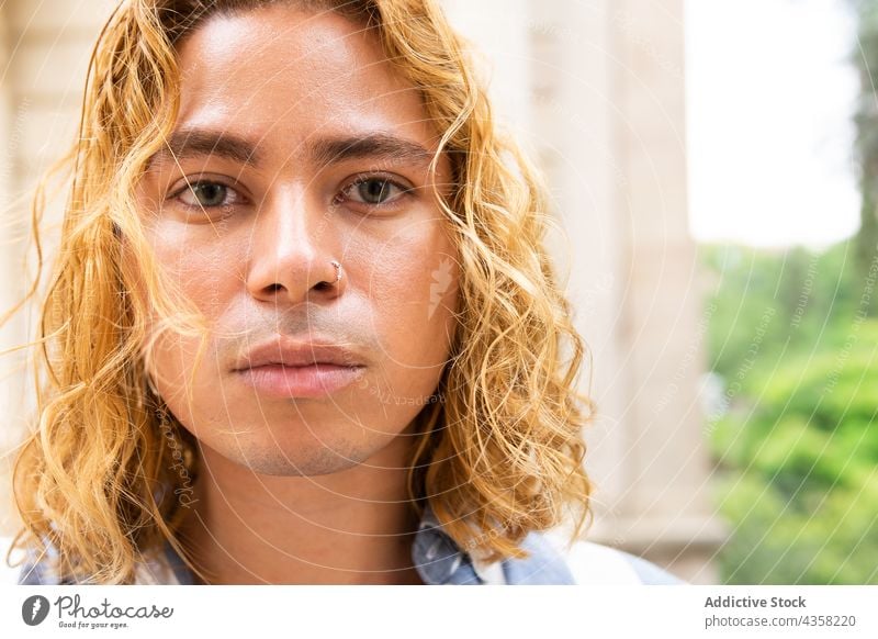 Trendiger Mann mit langen Haaren schaut in der Stadt in die Kamera lange Haare gewelltes Haar trendy Stil Großstadt Straße selbstbewusst gutaussehend urban