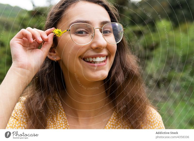 Lächelnde Frau mit Blume im Haar auf dem Lande Behaarung Landschaft Sommer Natur Blütezeit Wildblume heiter Glück gelb Feld charmant froh genießen angenehm