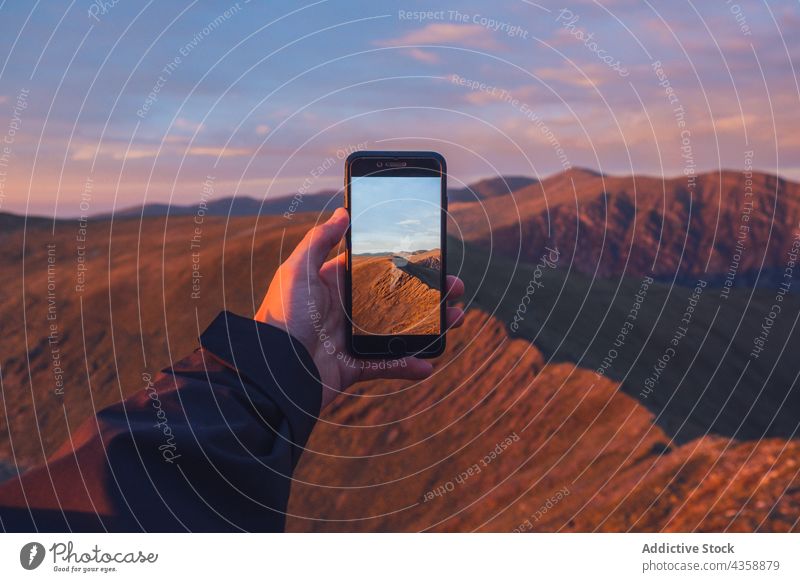 Crop-Reisender Mann, der abends mit seinem Smartphone ein Foto von den Bergen macht Wanderer fotografieren Berge u. Gebirge Hochland Ambitus Sonnenuntergang