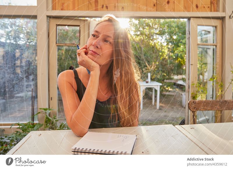 Lächelnde Frau, die im Gewächshaus Notizen in ein Notizbuch schreibt schreiben Notebook Notizblock Gärtner heiter Arbeit Pflanze Beruf eingetopft Blumentopf