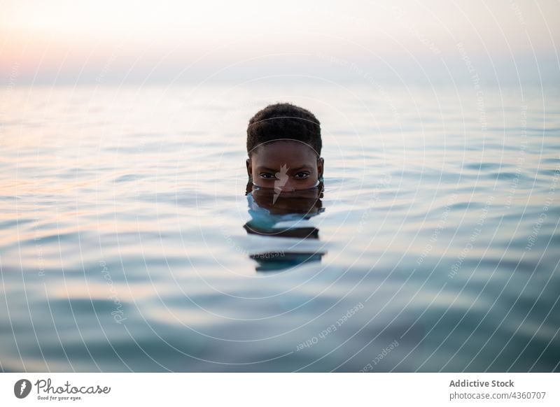 Schwarze Frau mit kurzen Haaren und halbem Gesicht im Meer MEER Wasser Hälfte Sonnenuntergang Rippeln Abend Sommer ethnisch schwarz Afroamerikaner ruhig