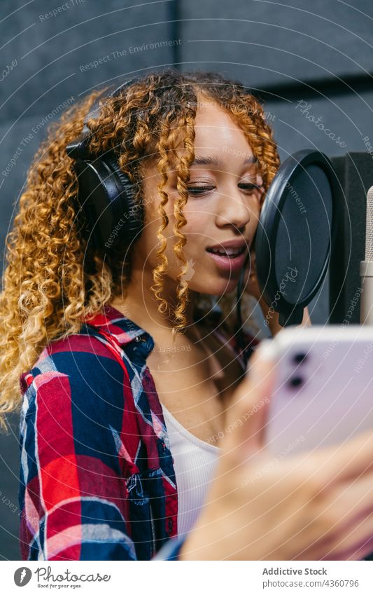 Lächelnder schwarzer Sänger mit Kopfhörer singt im Musikstudio Sängerin singen Gesang Headset Schallschutz Aufnahme Atelier Frau benutzend Gerät professionell