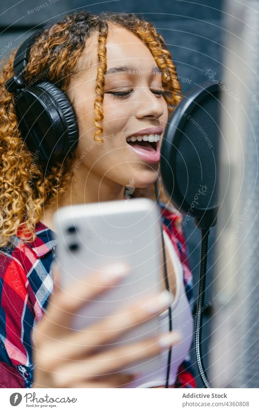 Lächelnder schwarzer Sänger mit Kopfhörer singt im Musikstudio Sängerin singen Gesang Headset Schallschutz Aufnahme Atelier Frau benutzend Gerät professionell