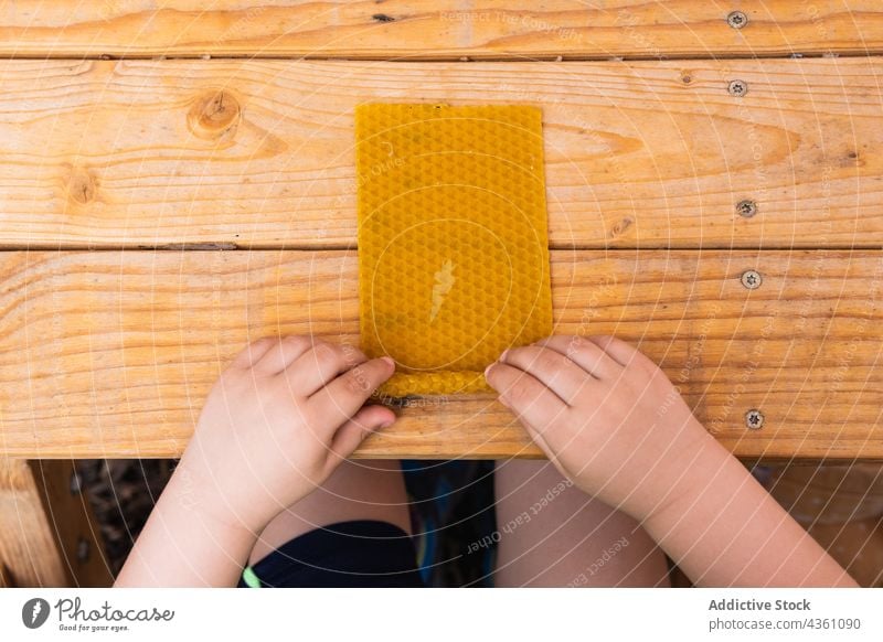 Ein Kind stellt am Tisch eine Kerze aus Bienenwachs her Wachs rollen handgefertigt kreieren Basteln kreativ hölzern vorbereiten Kindheit Hobby natürlich