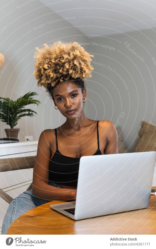 Schwarze Frau mit Laptop auf einem Stuhl sitzend beim Frühstück zuschauen Arbeit benutzend abgelegen online beschäftigt Morgen Gerät Browsen Apparatur heimwärts