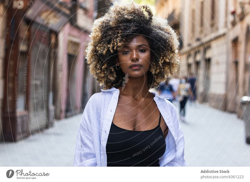 Wunderschöne Frau mit lockigem Haar steht auf der Straße ernst selbstbewusst selbstsicher Individualität cool Starrer Blick charmant Make-up Frisur Vorschein