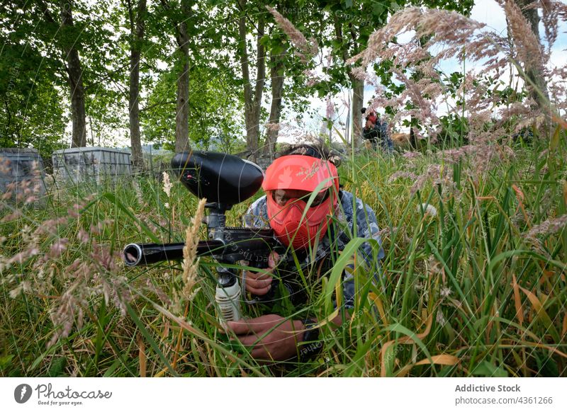 Anonymer Paintballspieler zielt auf Feinde, die sich im Gras verstecken spielen Männer Spiel zielen Team Spieler Pistole gegenüber unterhalten männlich Gegner