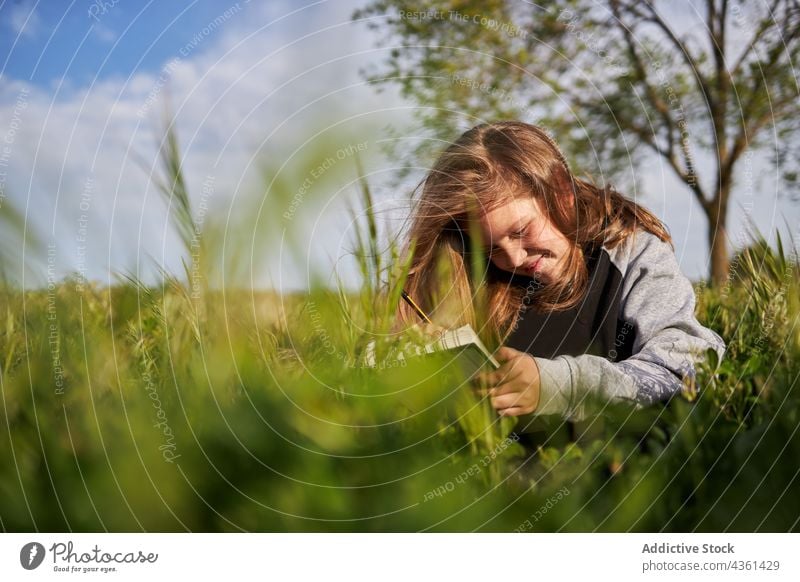 Fröhliches Mädchen, das auf einem Feld in ein Notizbuch zeichnet zeichnen Skizzenbuch Landschaft genießen kreativ Teenager Sommer Lächeln Glück Natur sitzen