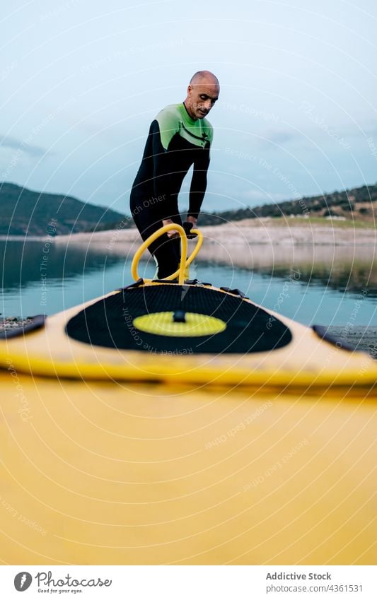 Mann pumpt Paddleboard vor dem Surfen auf Paddelbrett Pumpe SUP Zusatzplatine Surfer vorbereiten Meeresufer Neoprenanzug Strand männlich Surfbrett Sport