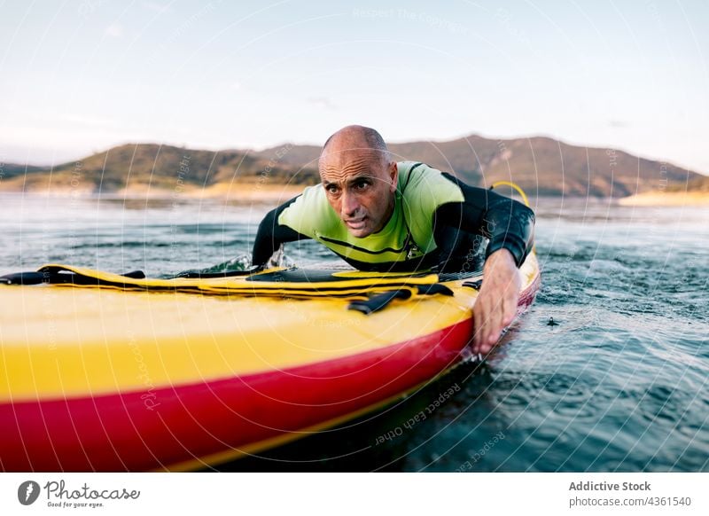 Mann übt Paddleboarding im Wasser eines Sees Paddel Holzplatte Lügen schwimmen Paddelbrett Aktivität üben Wassersport sportlich Schwimmer männlich aktiv