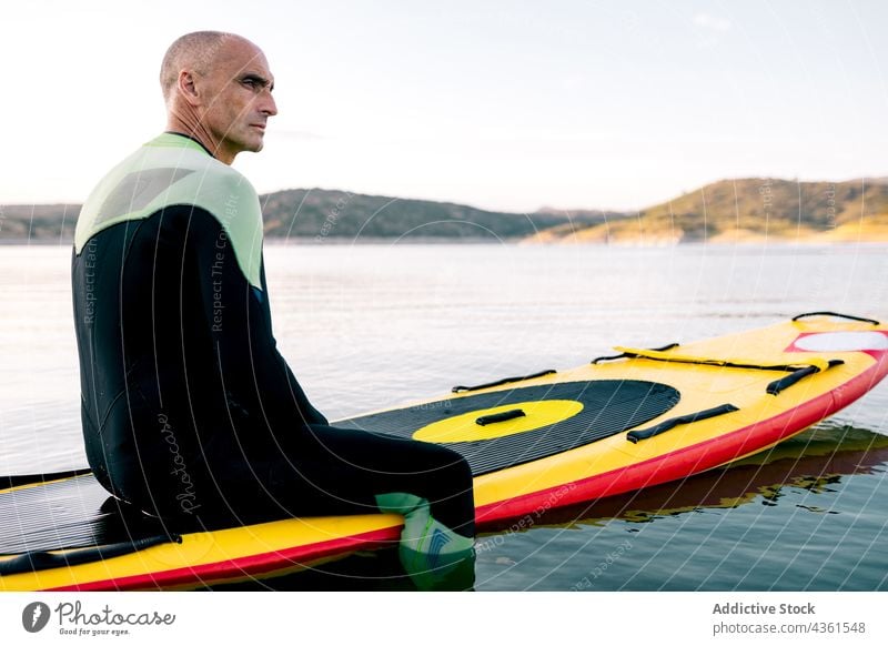 Mann auf Paddelbrett schwimmt auf See Holzplatte Sport besinnlich nachdenklich sitzen Aktivität üben Schwimmer männlich aktiv ruhen sportlich Erwachsener