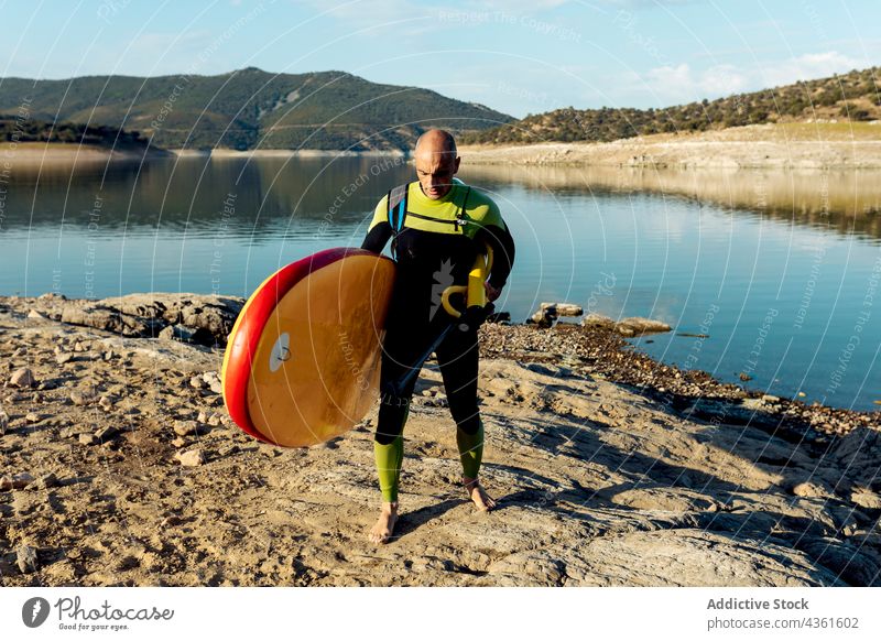 Mann mit Pumpe und Paddelbrett nach dem Surfen SUP Zusatzplatine Surfer Meeresufer Neoprenanzug Spaziergang beenden Strand männlich Surfbrett Sport Brandung