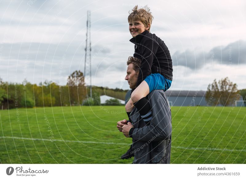 Vater und Sohn spielen Fußball auf einem Feld Zusammensein tragen Schulter Teenager Spieler Junge Aktivität Spaß haben Gras Eltern Vaterschaft Elternschaft