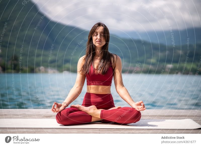 Flexible Frau meditiert in Lotus-Pose auf dem Pier meditieren Yoga padmasana See Gelassenheit üben Asana Wasser Gesundheit ruhig sitzen Vitalität Wohlbefinden