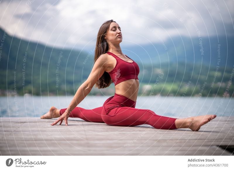 Flexible Frau in Front-Split-Pose sitzend und Yoga machend Dehnung beweglich Pier See üben ruhig Windstille Asana hanumanasana Harmonie Wasser Gelassenheit Kai