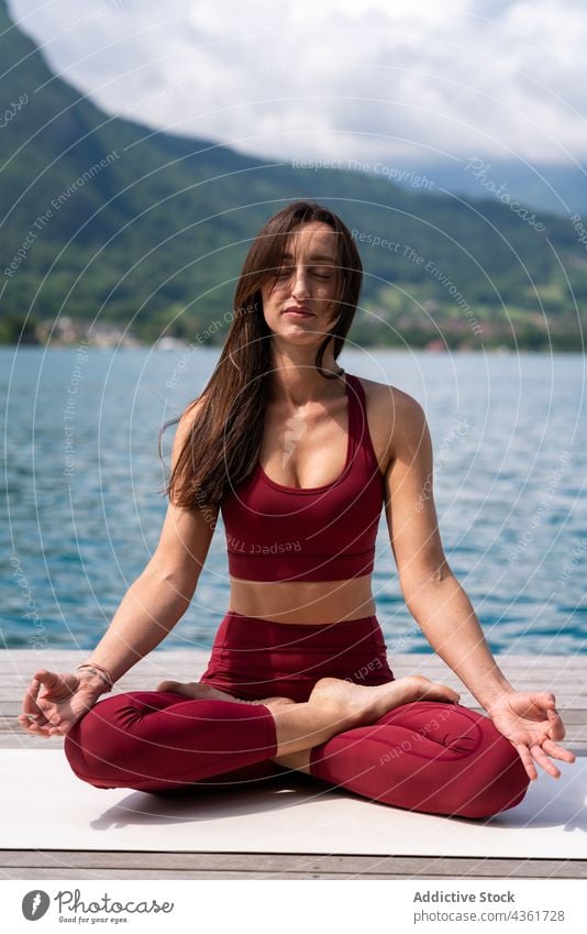 Flexible Frau meditiert in Lotus-Pose auf dem Pier meditieren Yoga padmasana See Gelassenheit üben Asana Wasser Gesundheit ruhig sitzen Vitalität Wohlbefinden