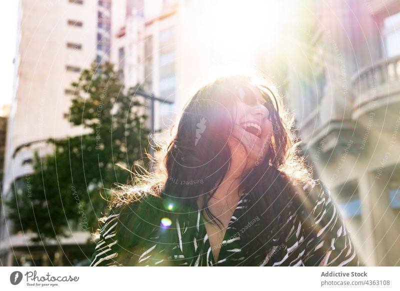 Stilvolle langhaarige Frau hat Spaß auf der Straße Behaarung Ohrringe Sonnenlicht Spaß haben Sommer urban Glück Mode jung Accessoire fliegendes Haar