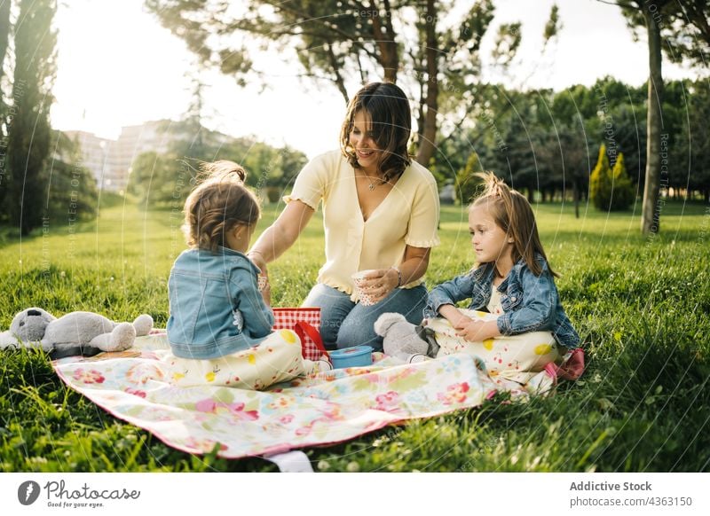 Fröhliche Mutter und Kinder beim Picknick im Park Zusammensein Sommer Glück Liebe Tochter Geschwisterkind trinken Tasse Mama Partnerschaft wenig Schwester