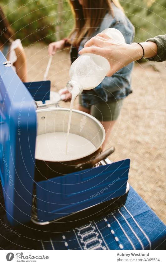 Frauen machen heiße Schokolade auf einem Campingkocher im Freien blau Küchenchef Koch Essen zubereiten Kochgeschirr kulinarisch flache Verlegung Lebensmittel