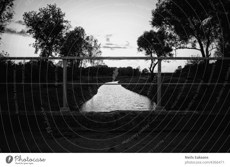 Schwarz-Weiß-Landschaft von Fluss und einige Bäume talen von alten Brücke. Klarer Himmel mit einigen Wolken. Helles Wasser. Brücke Eisengeländer im Vordergrund. Rechtecke.