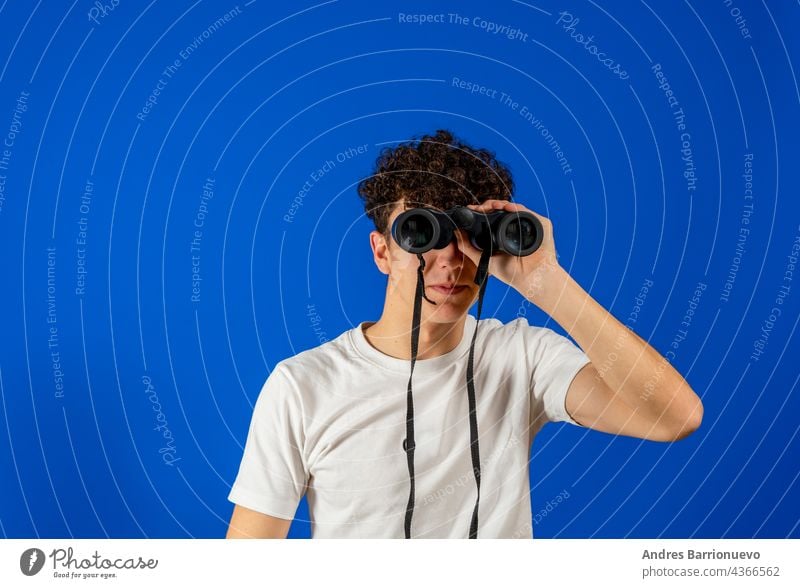 Junger Mann auf isoliertem blauen Hintergrund, der mit einem Fernglas in die Ferne schaut jung Golfloch Humor vereinzelt Aussehen Blick Model OK Person photogen