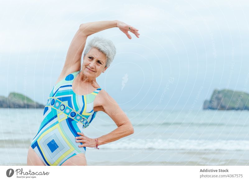 Alte Frau macht Übungen am Strand Senior Training Gesunder Lebensstil positiv Badeanzug MEER Stil Aktivität graues Haar alt Meer Lifestyle farbenfroh