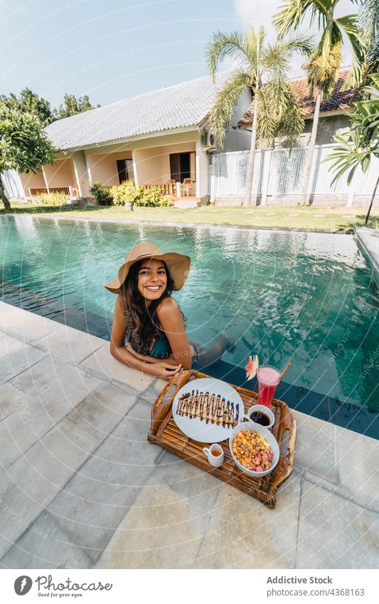 Zufriedene Reisende im Pool gegen leckeres Frühstück im Sommer Reisender geschmackvoll Resort Urlaub Lächeln Frau Porträt Kaffee tropisch Tourist Tablett heiter