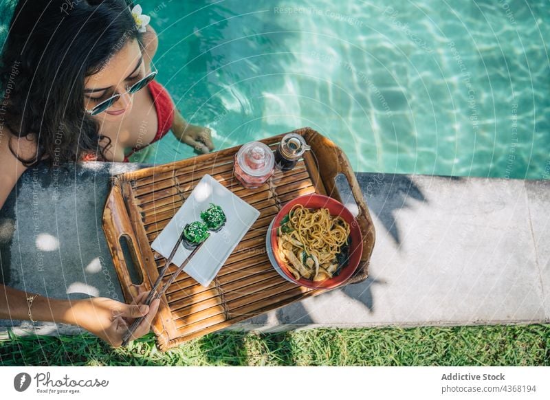 Crop-Reisende mit leckeren Sushi-Rollen am Pool im Resort Reisender Gunkan Nudel Hähnchen Mittagessen Meeresfrüchte Asiatische Küche Frau chuka Sonnenbrille