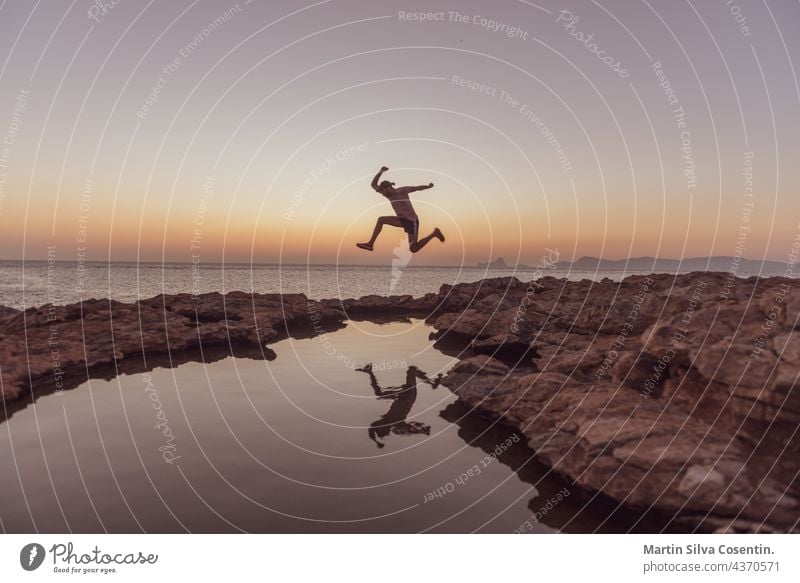 Junger Mann beim Sprung in den Sonnenuntergang in Can Marroig auf Formentera, Spanien Erwachsener Tier Hintergrund Balearen Strand schön Schönheit blau Boot