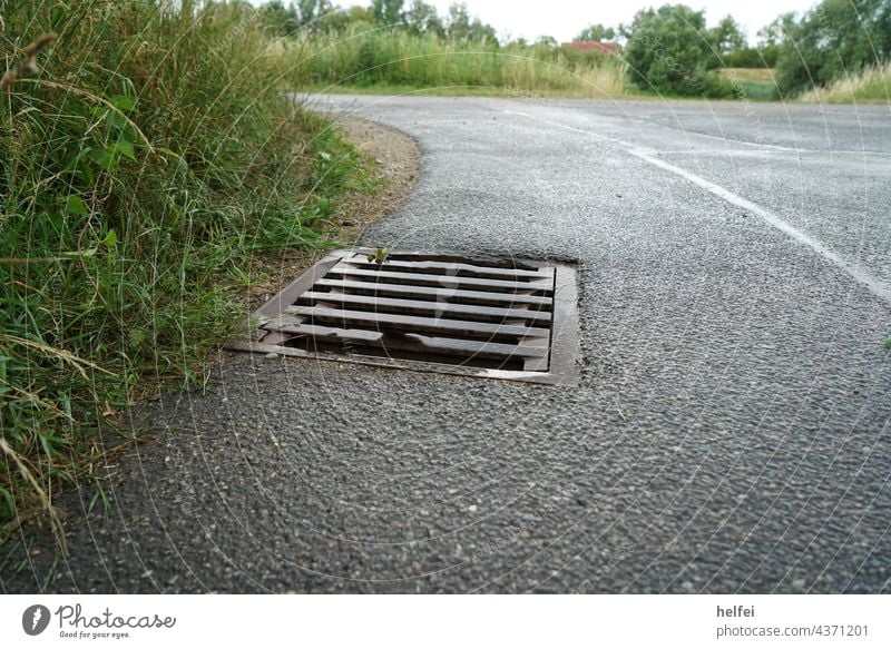 Detailaufnahme eines Kanaldeckels in der Kurve einer Teerstraße Gully Regen Gullydeckel Regenschauer Asphalt Deckel Fahrbahnbelag Abwasser Wasser reifenspur