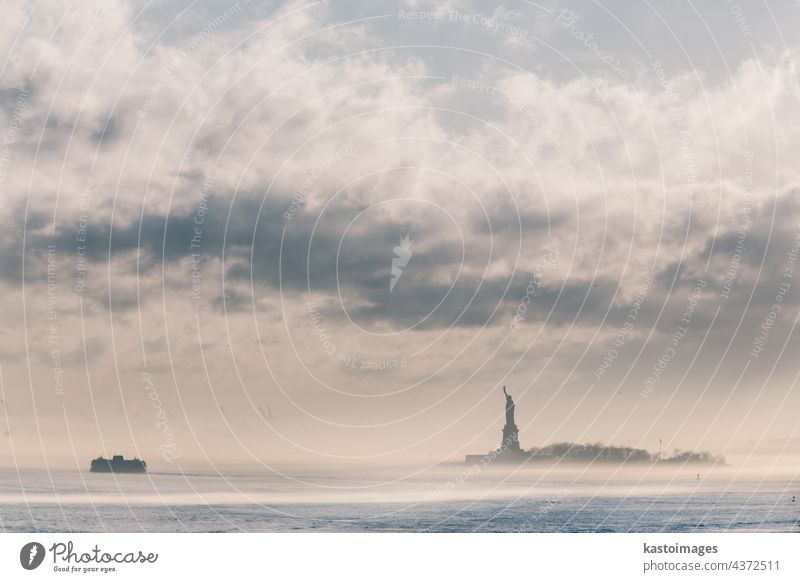 Die Staten Island Ferry fährt bei einem nebligen Sonnenuntergang an der Freiheitsstatue vorbei. Manhattan, New York City, Vereinigte Staaten von Amerika. Vertikale Komposition. Kopierraum.