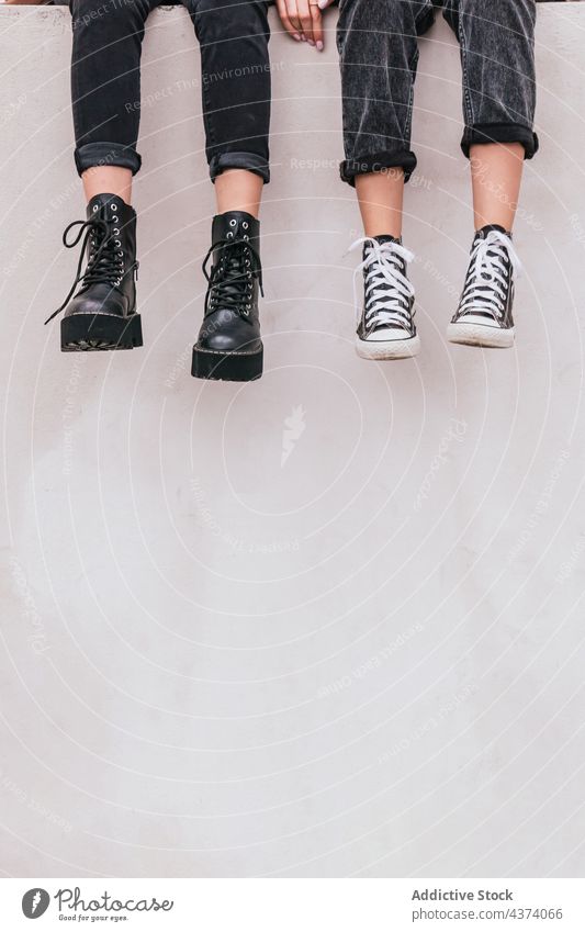 Crop-Freundinnen sitzen an der Wand Frauen Straße Stil urban ruhen Zusammensein Wochenende modern Stiefel Turnschuh Jeanshose lässig trendy Mode Schuhe