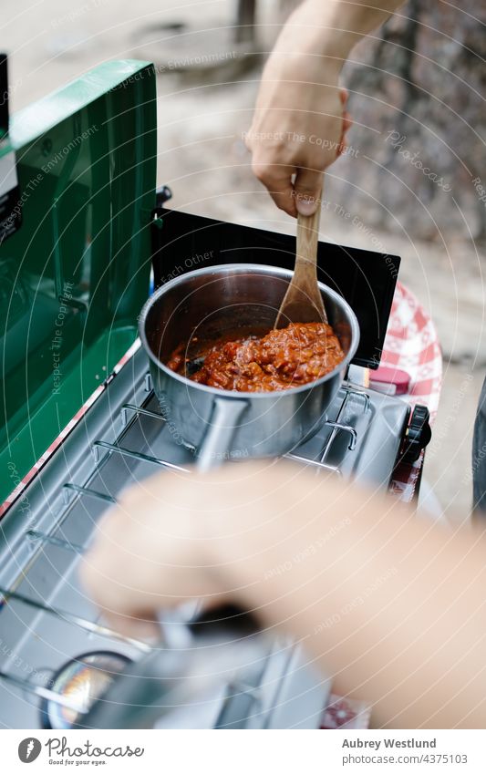 Mann kocht Chili auf einem Campingkocher in den Wäldern Baby blond Junge Kalifornien Lager Wohnmobil Campingplatz Kaukasier Peperoni Essen zubereiten Papa