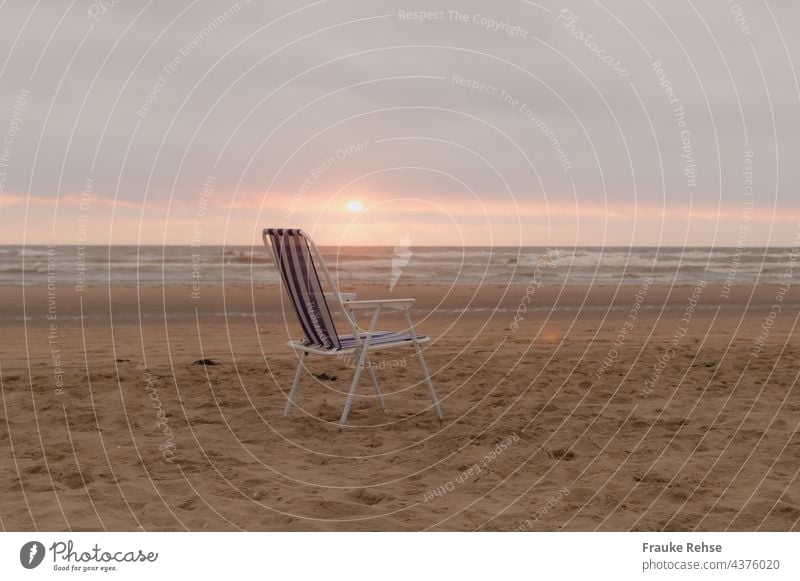 Blau-weißer Klappstuhl am Strand bei Sonnenuntergang blau gestreift Meerblick Nordsee Campingstuhl allein verlassen abends Weite Sommerurlaub Platz leer frei