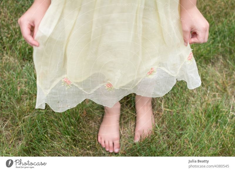 Kleines Mädchen modelliert Vintage-Brautjungfernkleid; das Mädchen hält das Kleid heraus, um die Blumenstickerei und den überschnittenen Rand zu zeigen