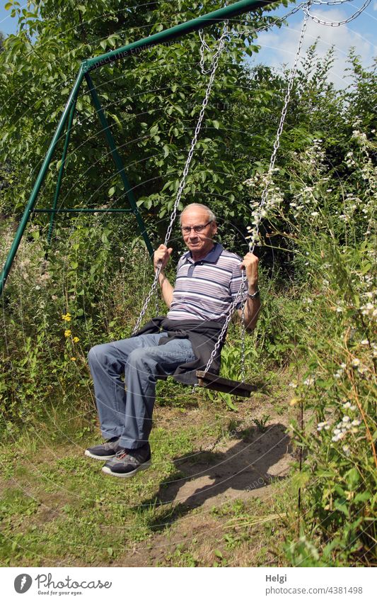 das Kind im Manne - Senior schaukelt bei Sonnenschein in einem Blumengarten Mensch 70+ Schaukel schaukeln Garten Licht Schatten Freude Spaß schönes Wetter