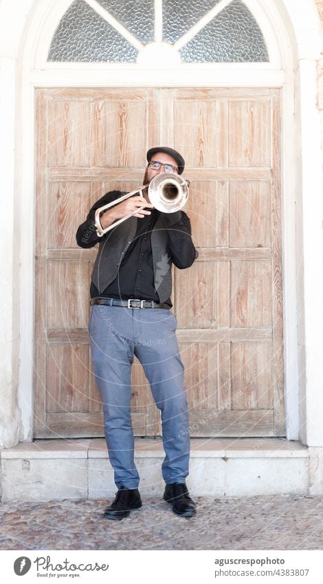 Jazzmusiker mit Brille und Bart spielt Posaune auf der Straße stehend Musiker Spielen Stehen Verschlussdeckel englische Kappe Jacke Türöffnung Mezzanin Arkaden