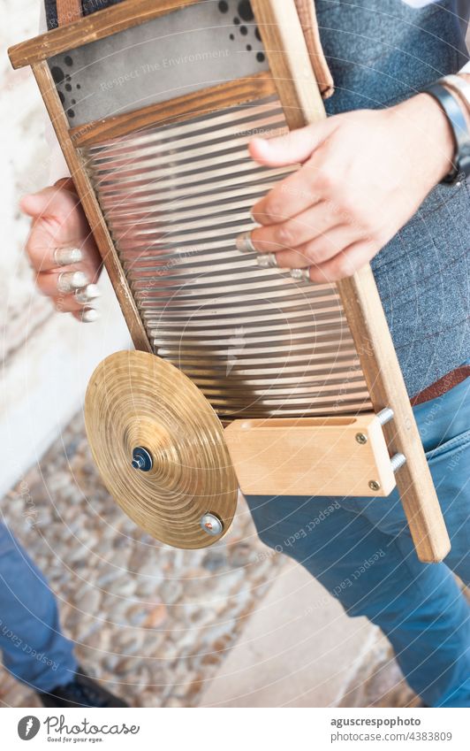 Nahaufnahme eines Mannes, der auf einem Waschbrett auf der Straße ein Jazzinstrument spielt. Das Instrument ist zu sehen, zusammen mit dem Becken, dem Holz und den Fingerhüten, mit denen es gespielt wird.