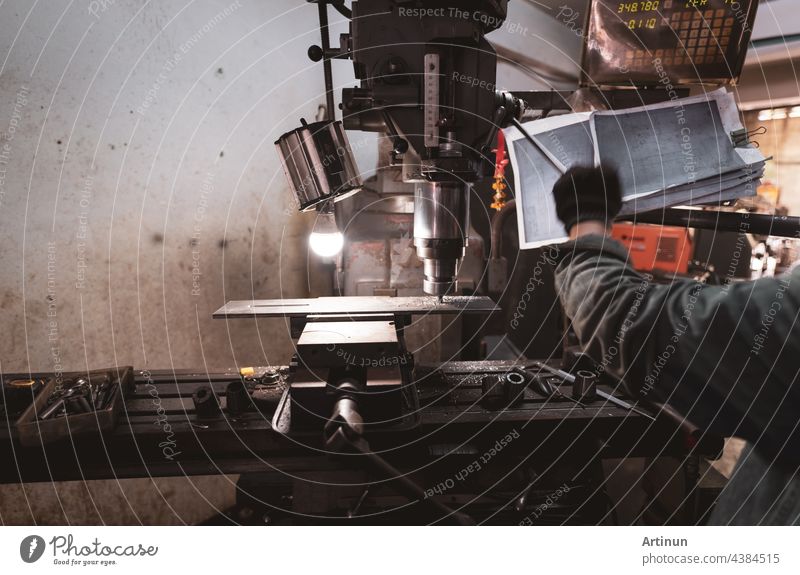 Fräsmaschine in der Nähe eines Arbeiters mit Handschuhen. Werkzeug zum Schneiden von Metallwerkstücken. Vertikale Fräsmaschine mit Hartmetallfräser. Stahlverarbeitende Industrie. Fräsvorgang. Metallbearbeitung.