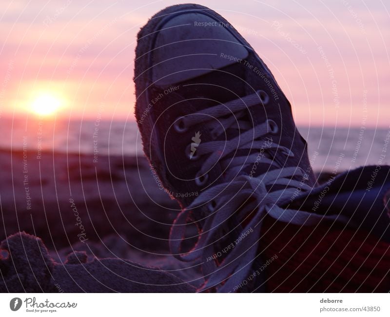 Unterhalten Sie sich mit Chuck Taylor Taylor All Stars am Strand mit der untergehenden Sonne im Hintergrund. Sonnenuntergang Schuhe Chucks Meer Wolken