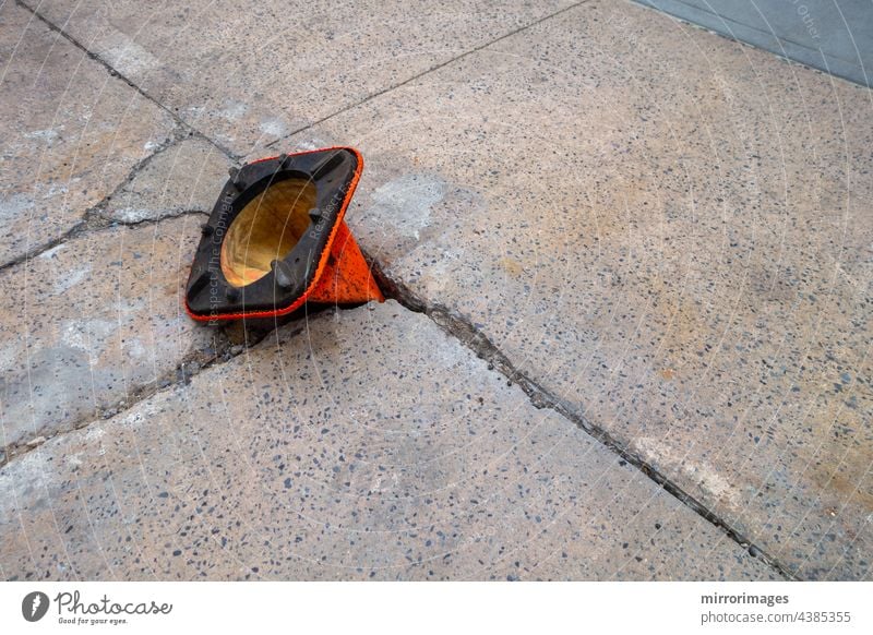 kaputter, verwitterter Bürgersteig mit Schlagloch und orangefarbenem Kegel, der verkehrt herum im Loch liegt Asphalt Hintergrund schwarz blau