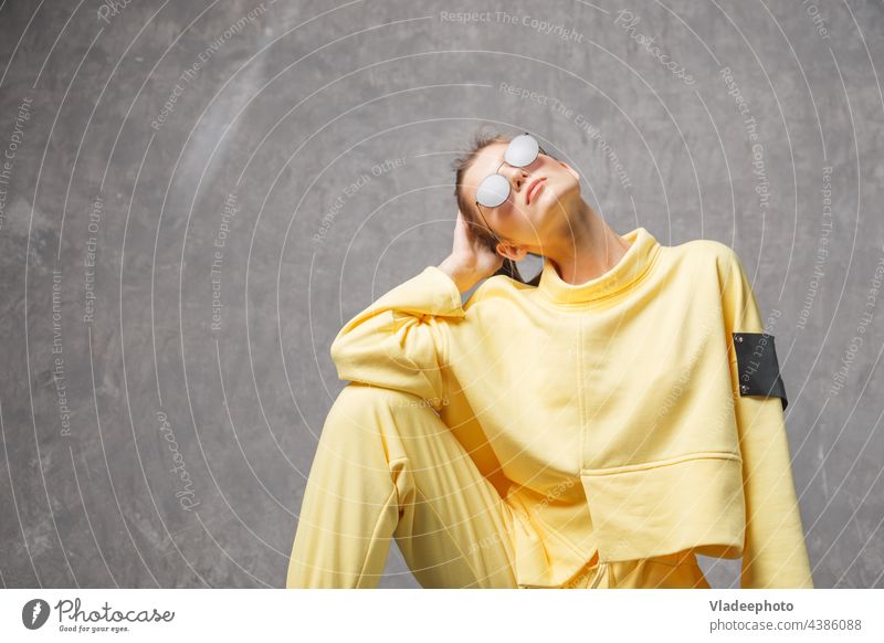 Junge Frau in gelbem Sweatshirt und Sonnenbrille auf grauem Hintergrund Porträt Model jung Mädchen Nahaufnahme Atelier Behaarung Gesicht Schönheit sinnlich