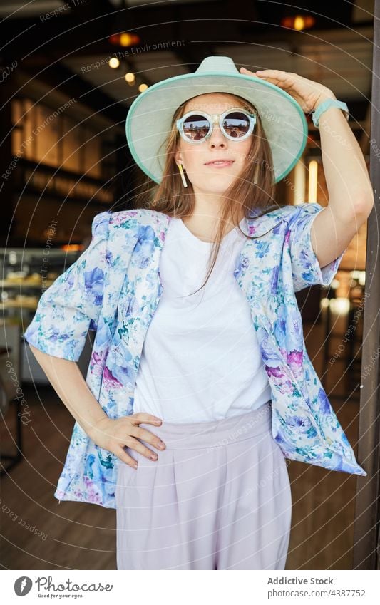 Lächelnde Frau mit Hut vor einem Gebäude mit Backsteinmauer Mode Stil Sonnenbrille freundlich herzlich Stadt Porträt Backsteinwand stylisch anhaben Ornament